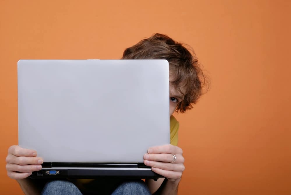 Person hiding behind silver laptop with orange background representing the vulnerablity of writing doula website copy